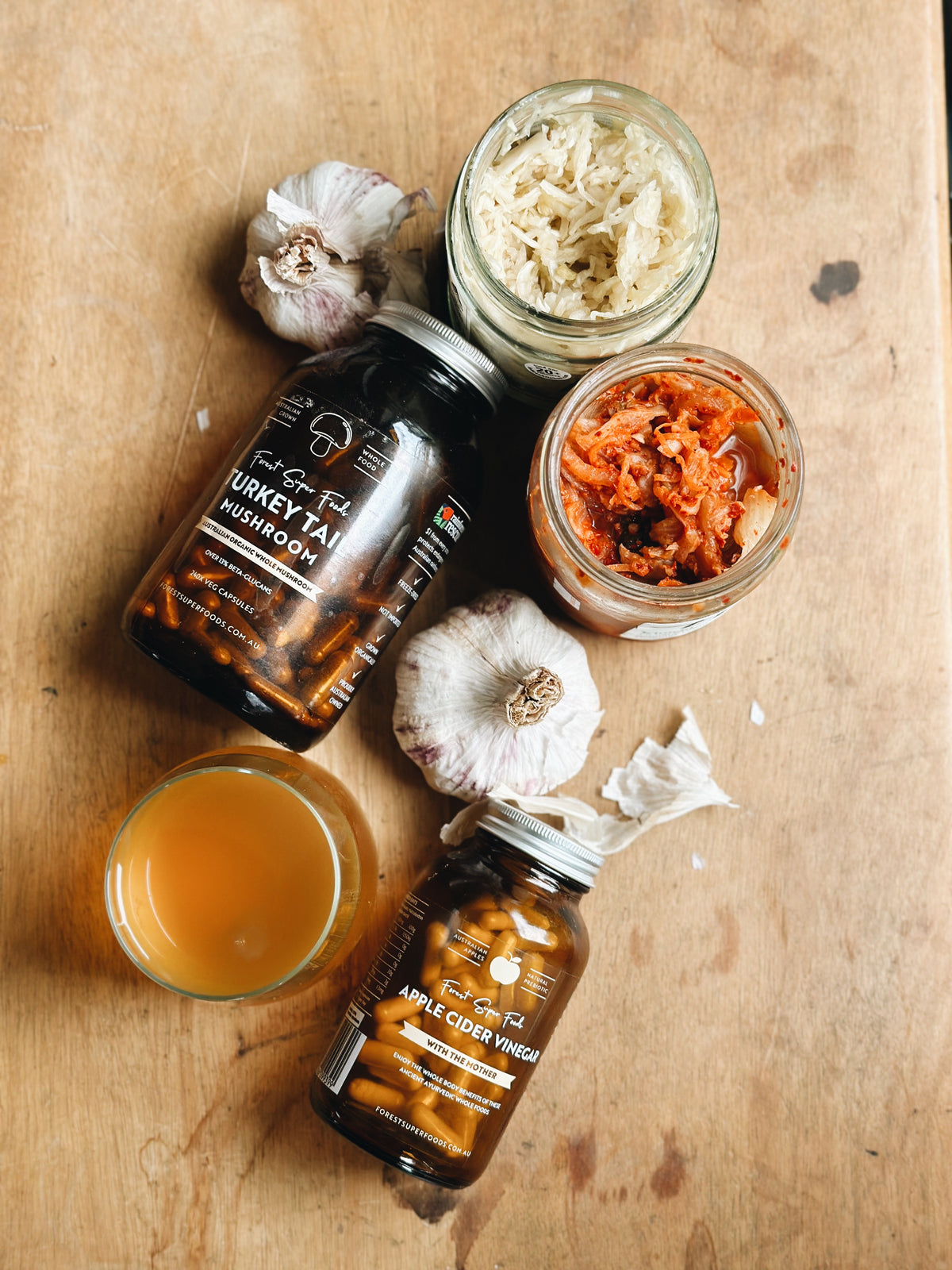 Australian Apple Cider Vinegar Capsules bottle on wood surface with garlic cloves and fermented vegetables by Forest Super Foods