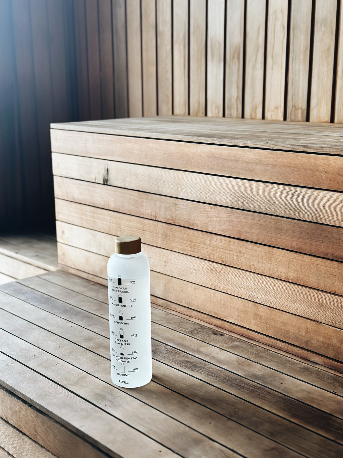 Borosilicate Glass Drinking Bottle with motivational time markers placed on wooden bench in bright natural light